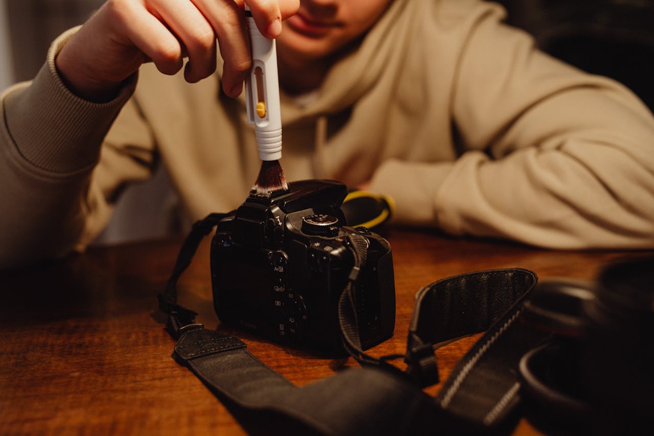 A person carefully cleaning a camera with a brush, emphasizing photography maintenance.